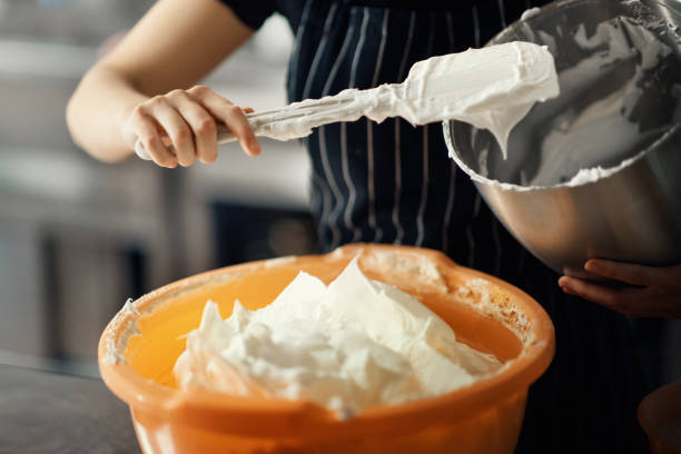 Closeup of unrecognizable women mixing a cake batter inside of a big plastic bowl.