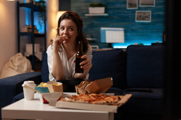 istock Woman relaxing on sofa watching television while drinking craft beer and eating potato chips 1493474943