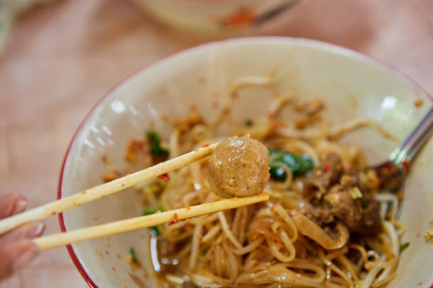 Pick up meatball by chopsticks on hot noodles in a bowl