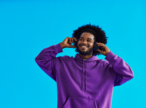 Young black man with a afro hairstyle, beard and a mustache wearing a purple hoodie, standing with his headphone on whilst smiling with dental braces with copy space, stock photo
