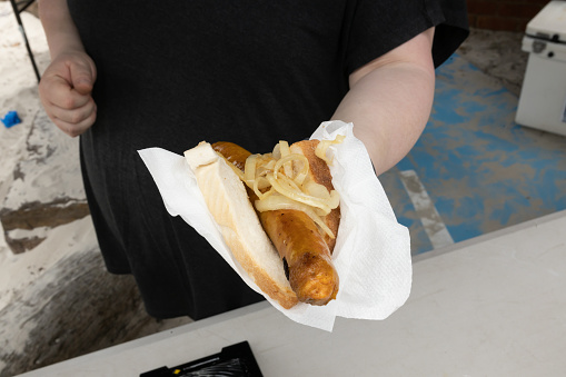 An unrecognisable person handing over a sausage in bread at a traditional australian bbq sausage sizzle