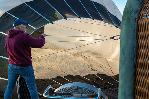 Men prepare a large hot air balloon for flight, one of them adjusts the folds of nylon material inside the balloon.