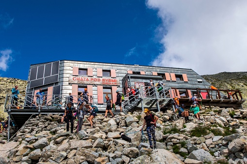 Rysy, Slovakia – August 10, 2022: A group of people ascending a set of stairs leading up to a mountain-side building.