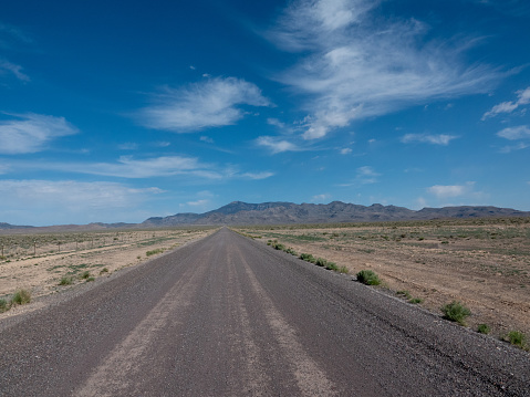 Straight empty desert gravel road and mountains, western Utah.