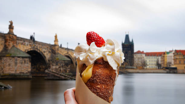trdelnik, with cream and strawberry, Charles Bridge view in Prague. Typical local cuisine The trdelník, also called trdlo, trozkol, also known as Bohemian sleeve, is a typical dessert of Hungarian and Slovak cuisine trdelník stock pictures, royalty-free photos & images