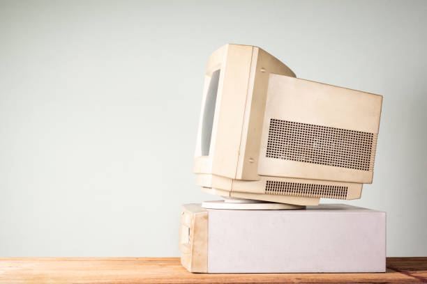 Side view of old and obsolete computer on old wood table with coloured concrete wall background