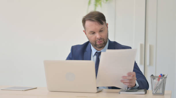istock Reading Document by Businessman and Working on Laptop 1493506941