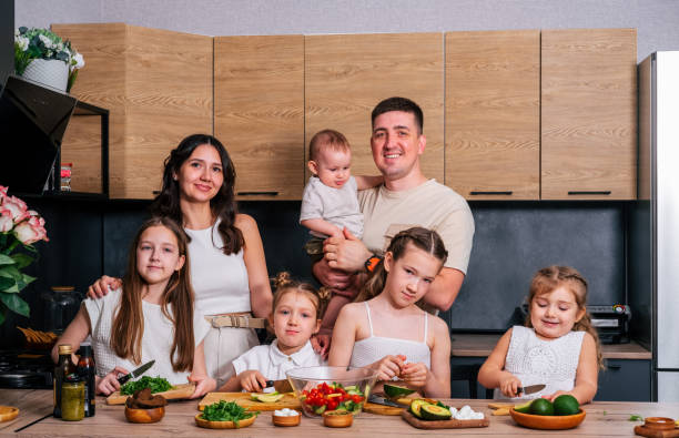 una famiglia numerosa - mamma, papà, 4 figlie e un bambino insieme preparano un'insalata per pranzo in una cucina moderna. grande concetto di famiglia insieme. - 6 11 mesi foto e immagini stock
