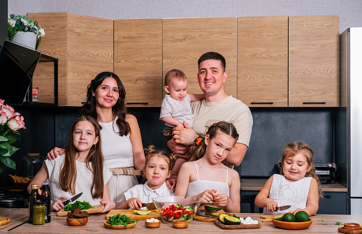 A large family - mom, dad, 4 daughters and a baby son together prepare a salad for lunch in a modern kitchen. Big family together concept.