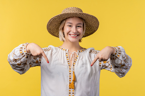 Ukrainian woman pointing down to advertising area. Yellow background. Young lady asking to click to subscribe below. Copy space for your commercial idea, promotional content. High quality photo