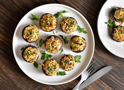 Stuffed mushrooms with cream cheese, bread crumbs and nuts on plate over wooden background. Top view, flat lay