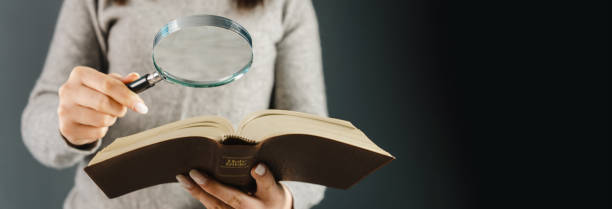 Woman looking at a bible with a magnifying glass stock photo