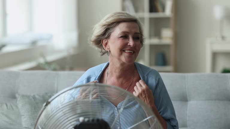 Happy lady sitting at fresh cool air blowing from fan
