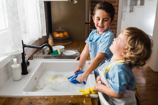 Children having fun washing and playing with dish soap foam and gloves  in the kitchen sink