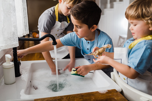 Children having fun washing and playing with dinosaur toy in the kitchen sink