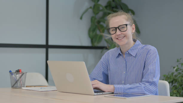 istock Young Woman Smiling at Camera while Working on Laptop 1493522679