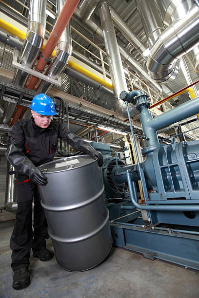 Oil Worker  inside refinery dealing with silver  barrel stock photo