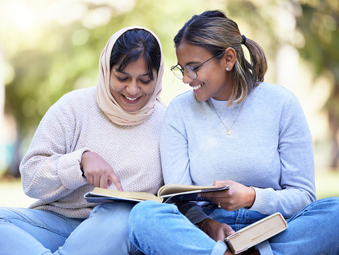 Study friends, park reading and outdoor woman students with university textbook and books. College female, girl friend and muslim young person learn on a outdoor campus with a smile from studying