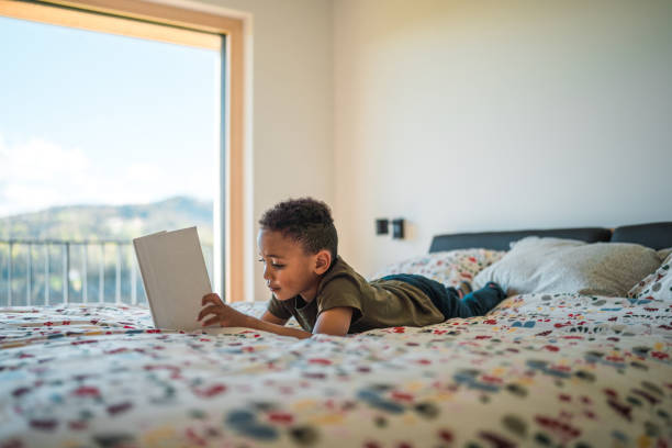 istock Lovely Mixed Race Boy Lying On The Bed Reading A Book 1493527420