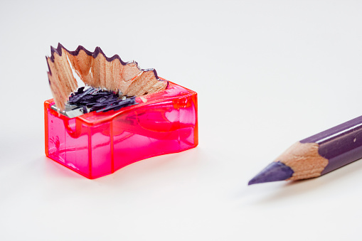 A black color wood pencil crayon placed beside a s shaped pencil shavings and a pencil sharpener
