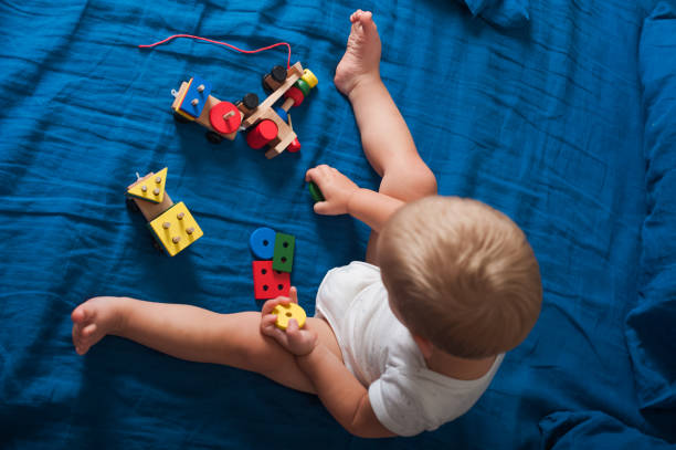 istock Toddler boy plays with wooden constructor train on bed close-up. 1493533955