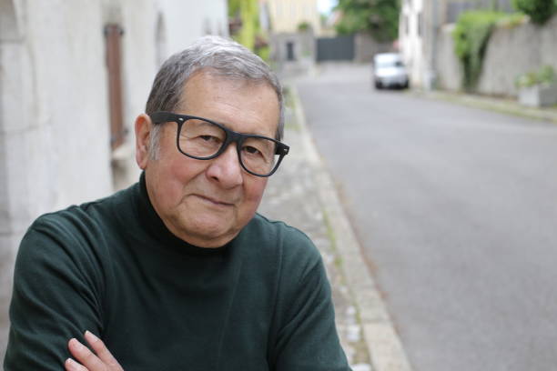 A senior ethnic businessman in his seventies is posing with his arms crossed. He wears an elegant green turtle neck sweater and eyeglasses.