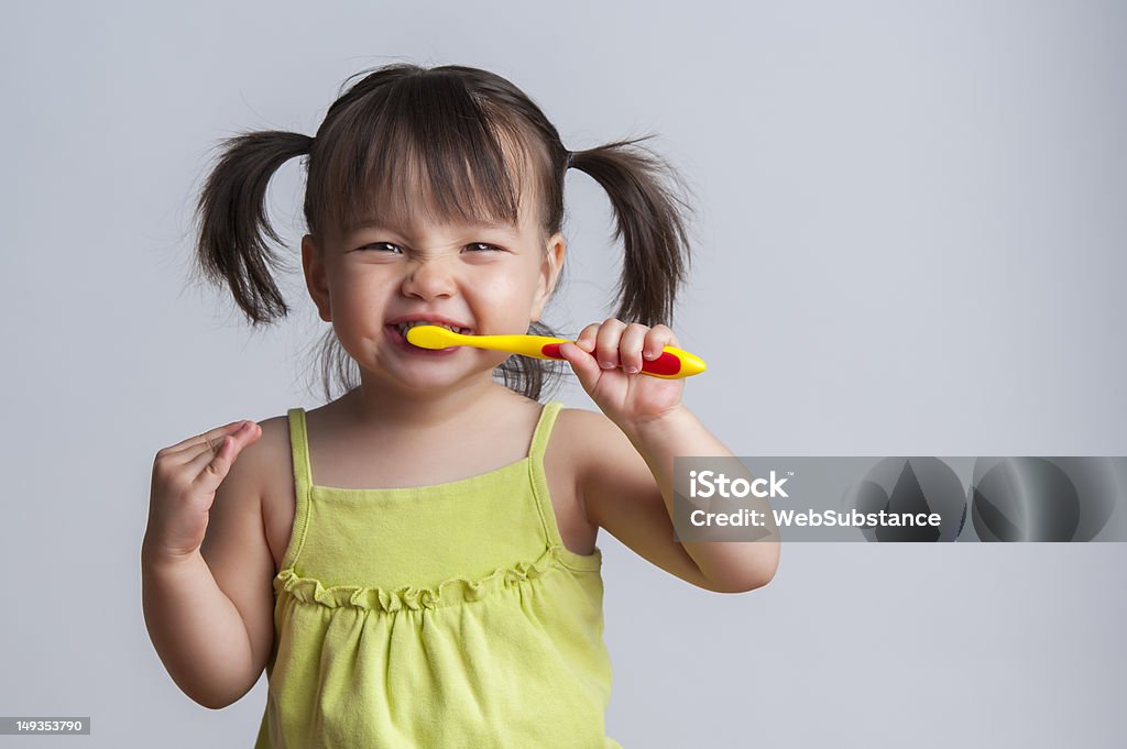 Young girl brushing teeth with yellow toothbrush Toddler smiling while brushing her teeth Child Stock Photo