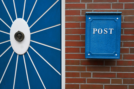 Door and mailbox in similar colours. The blue door is decorated with a white oval and fanning stripes and an ornament in the middle