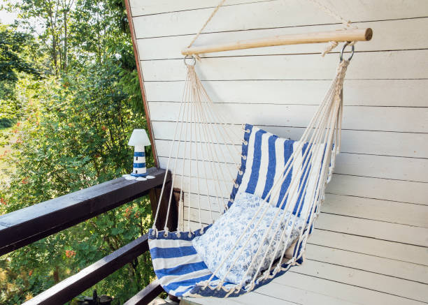 青と白の縞模様の紐と織物のハンモック吊り椅子、白い塗装された木の板の背景。夏の日に屋外でリラックスできるホームコテージバルコニー。