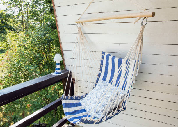 istock Blue and white striped pattern string and textile hammock hanging chair, white painted wooden board background. Relaxing home cottage balcony outdoors on summer day. 1493543597
