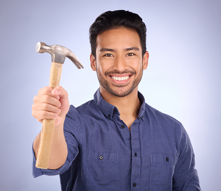 Construction, showing and portrait of an Asian man with a hammer isolated on a studio background. Building, happy and builder with a tool for repairs, maintenance and handyman work on a backdrop