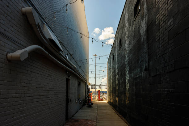 Shaded alley and back entrance of houses with garbage bins lead to waterfront in Downtown district in Newport News, Virginia