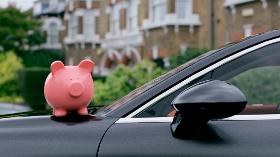 Pink piggy bank stands the hood of car parked outside. Concept of saving money on buying a car, insurance or car ownership.