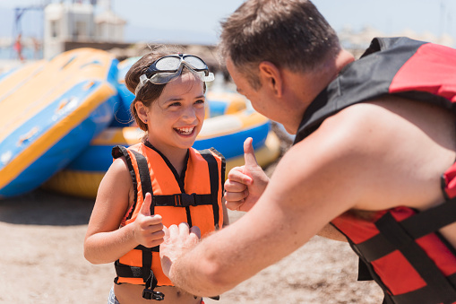 Happy teenage girl smiling and looking at her father adjusting her life vest