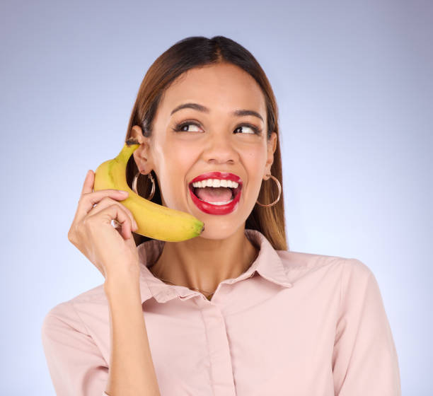 istock Woman, studio and banana phone call for hello, happiness or comic communication for makeup, beauty or fashion. Gen z girl, funny chat or conversation with mobile fruit for diet, wellness or cosmetics 1493569590