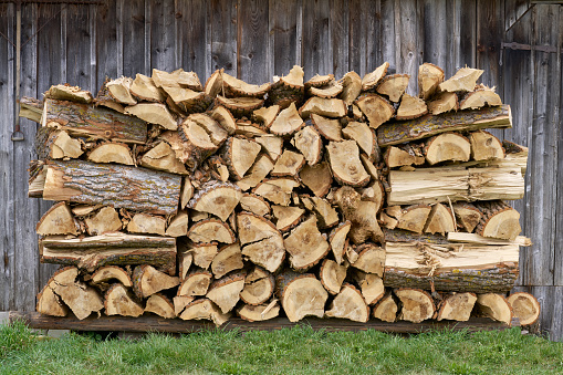 Rustic wood pile in the grass in front of the gray old wooden wall of a barn