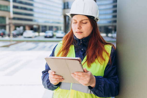 istock Young architect woman in white hardhat and safety vest using digital tablet outdoors. Female construction engineer. Engineering application, Modern exterior. 1493571211