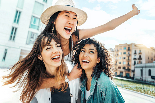 Three young multicultural women having fun on city street outdoors - Mixed race female friends enjoying  summertime vacation together - Friendship concept with happy girls laughing out loud