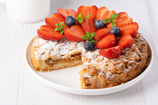 Sweet cake with strawberries on plate on white wooden background.