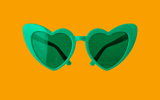 Heart-shaped green sunglasses on orange background. Funny sun glasses for Saint Patrick s day.