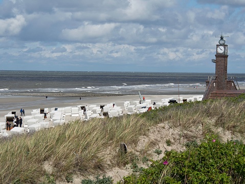 A sandy shore with multiple beach chairs and a clock tower. Wangerooge, Germany.