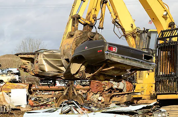 A large excavator crushing and piling discarded autos for metal recyling.