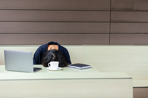 Tired freelancer woman sleeping on table in cafe