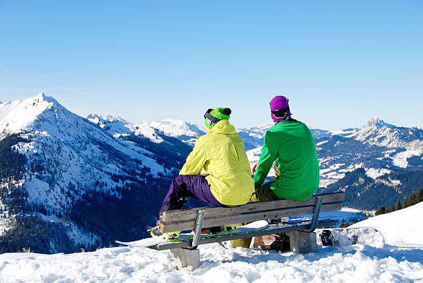 Two snowboard friends sitting on bench in snowy alps