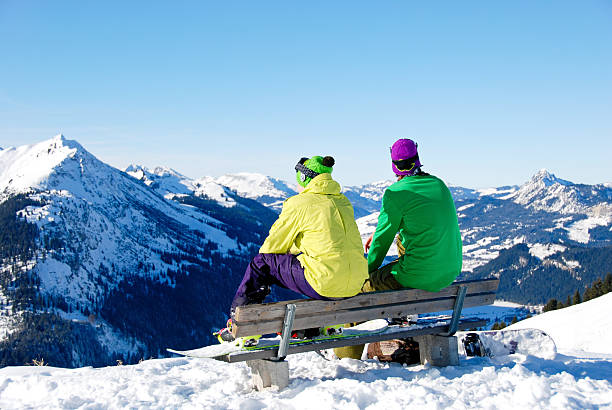 Two snowboard friends sitting on bench in snowy alps stock photo