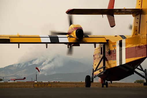A Super Scooper starts its engines at an airport with a wildfire in view, preparing to help fight the fire.