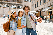 Three smiling tourists taking selfies in the old town square