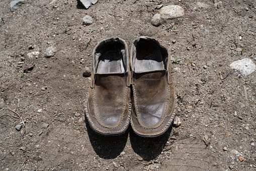 Looking down at weathered moccasins on bare soil.