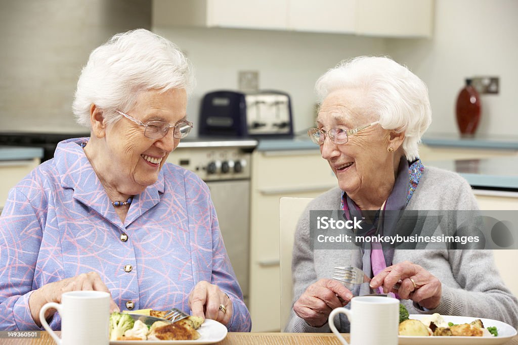 Two gray haired friends enjoying a meal together Senior women enjoying meal together in kitchen at home Senior Adult Stock Photo