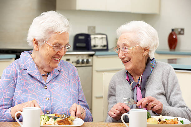 Two gray haired friends enjoying a meal together Senior women enjoying meal together in kitchen at home 80 89 years stock pictures, royalty-free photos & images